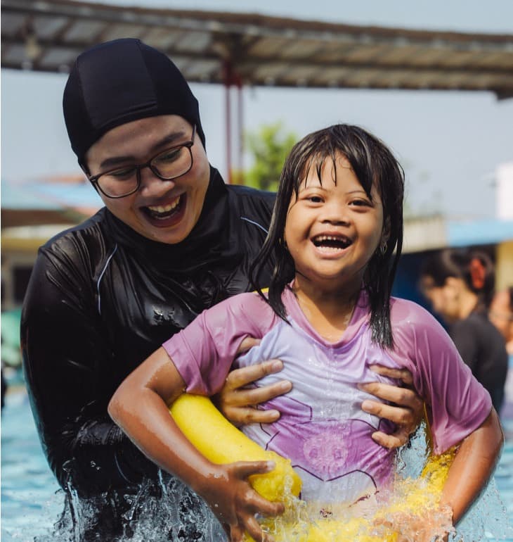 Caregiver and young girl with autism smiling happily in aquatic therapy