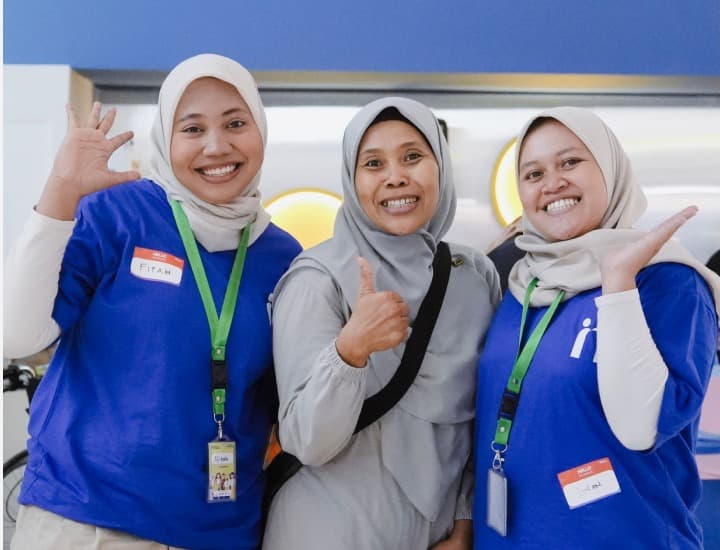 Three smiling volunteers in blue shirts giving thumbs up