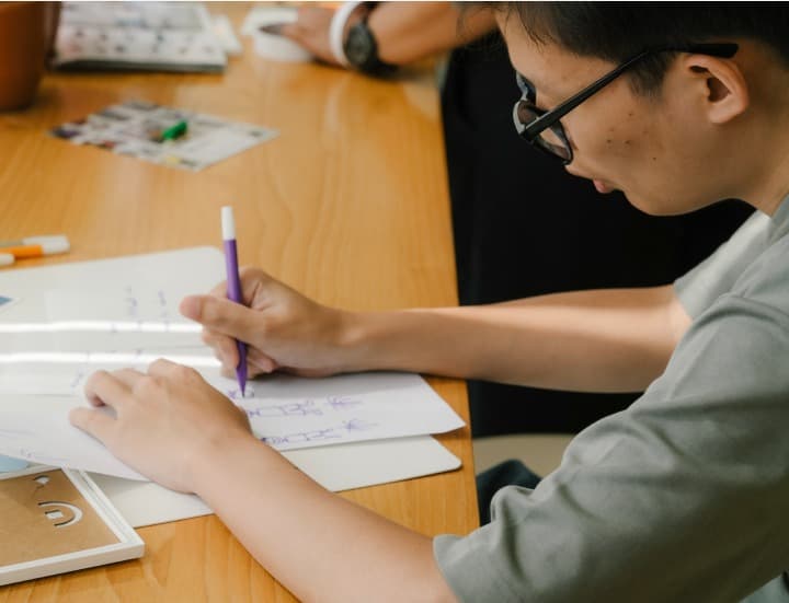 Person sketching with purple pencil on notebook
