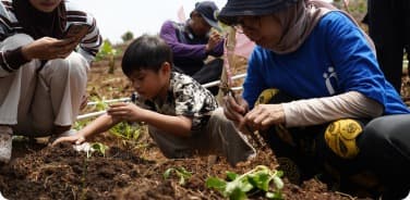 Young students and mentor planting seeds into garden soil